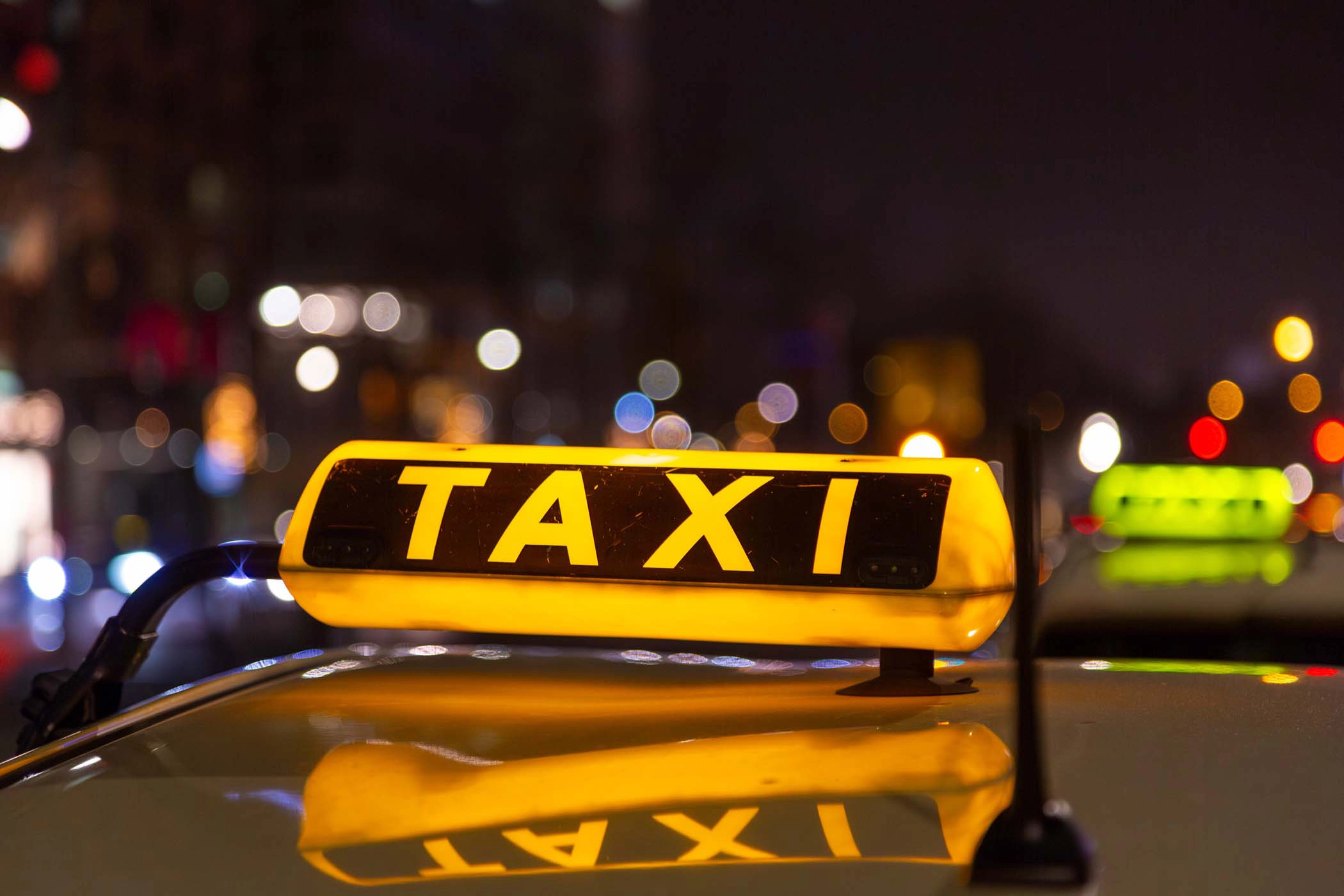 Professional photo of a taxi roof sign that is glowing yellow, it reads "TAXI"